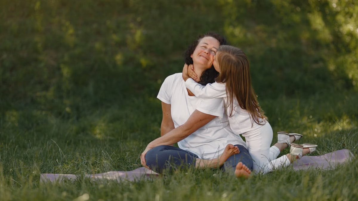 A joyful moment between mother and daughter hugging on a grassy field.